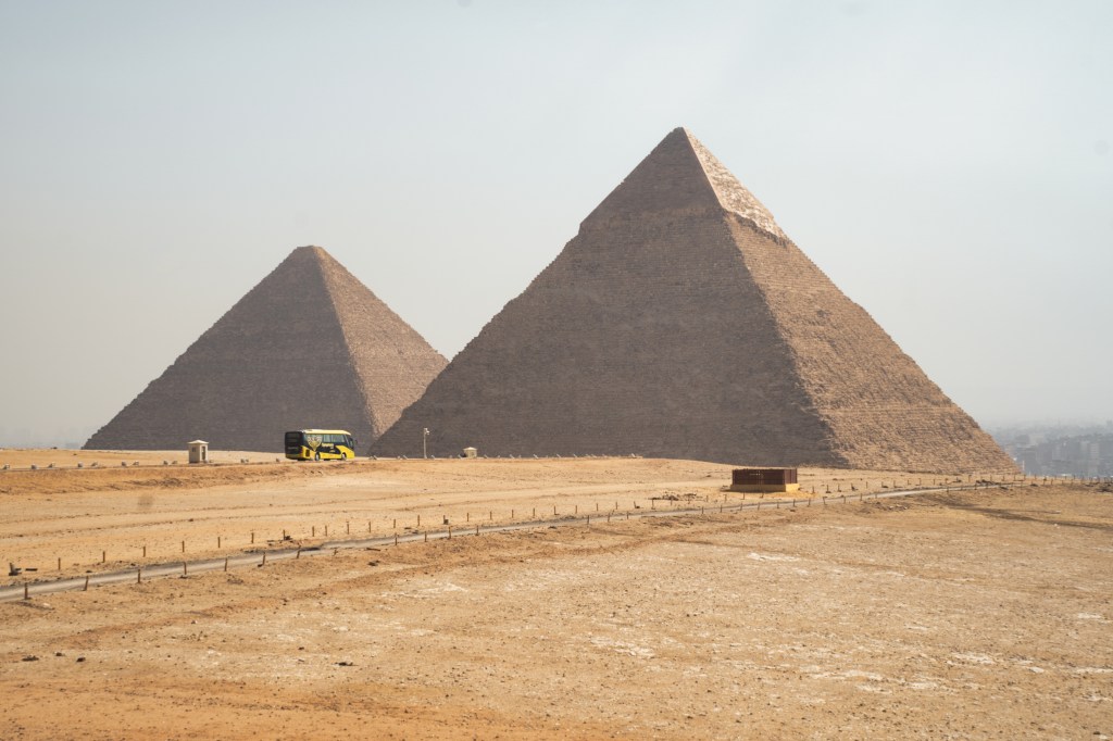 Two pyramids rising above the sandy Giza plateau beneath a pale sky.