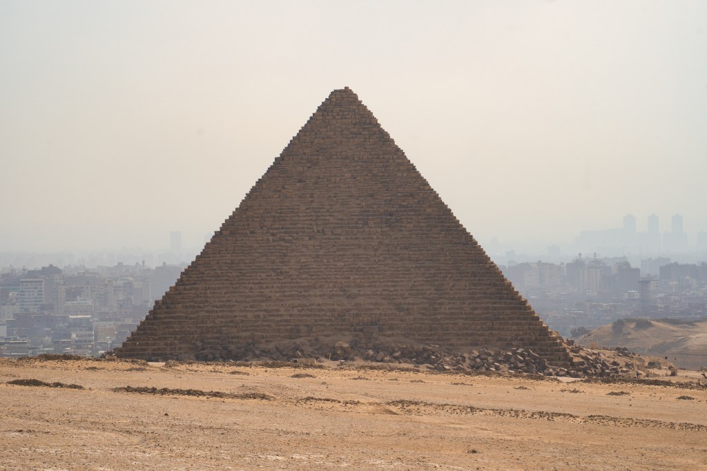 A pyramid standing against the hazy skyline of the city beyond.