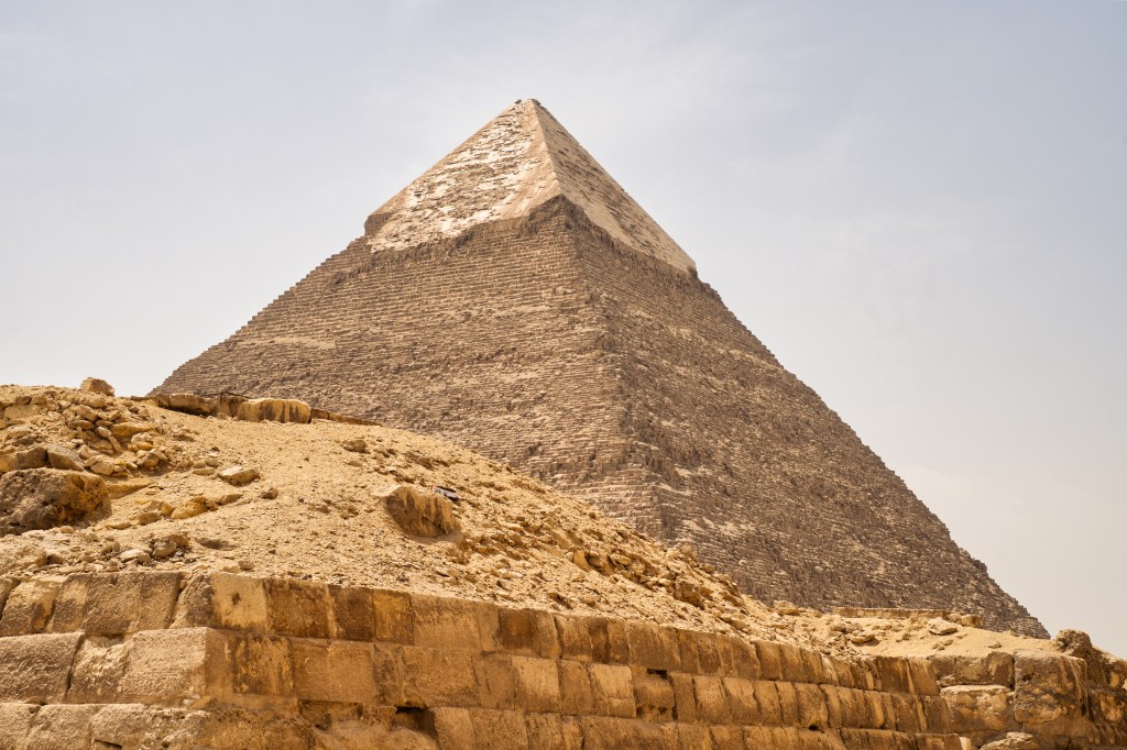 A pyramid with a smoother upper section rising behind weathered stone ruins.