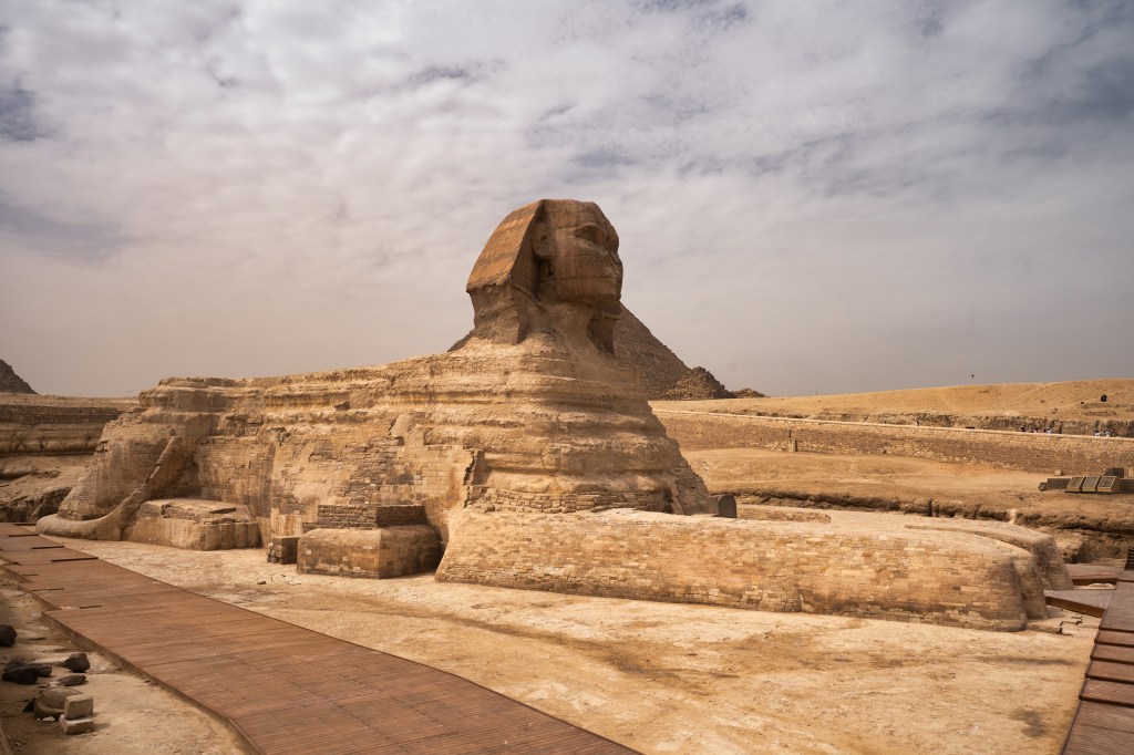 The Great Sphinx surrounded by stone walls beneath a clouded sky.