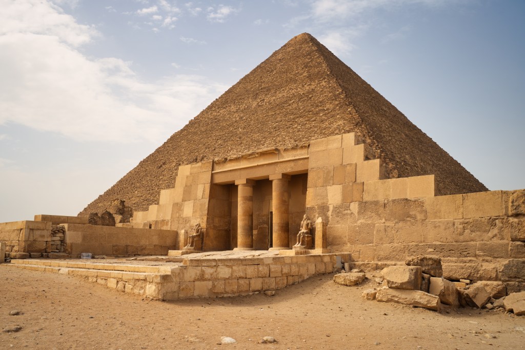 Stone temple entrance and statues at the foot of a pyramid.