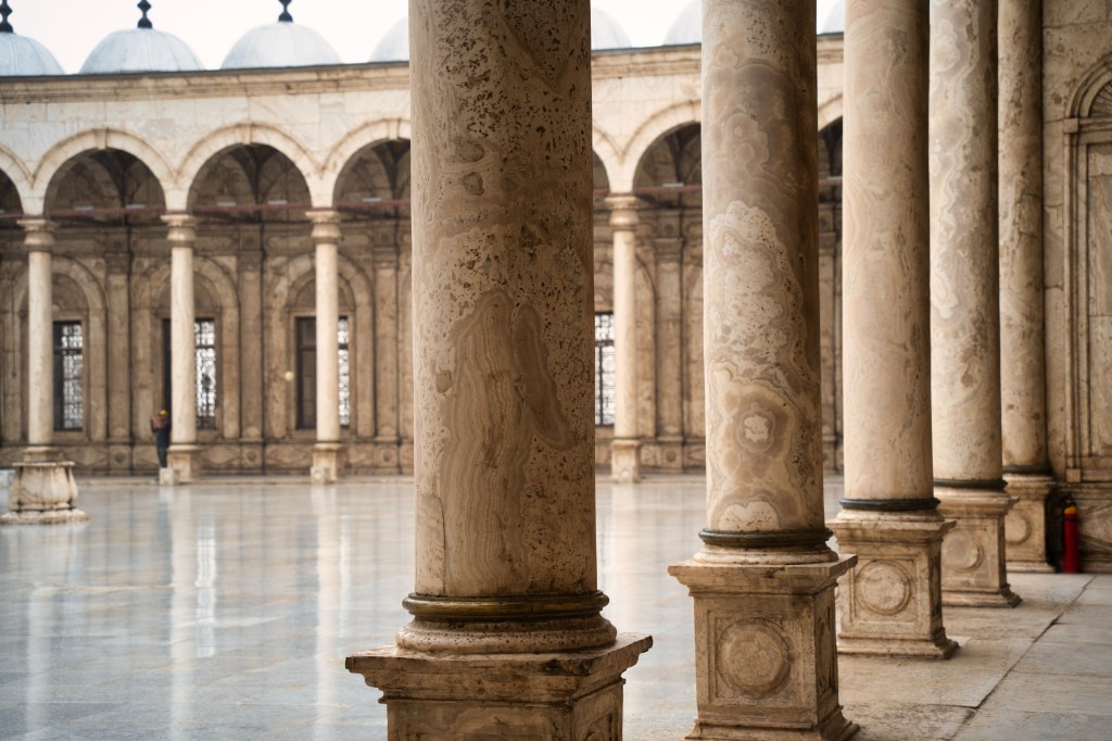 Stone columns framing a mosque courtyard lined with arches.