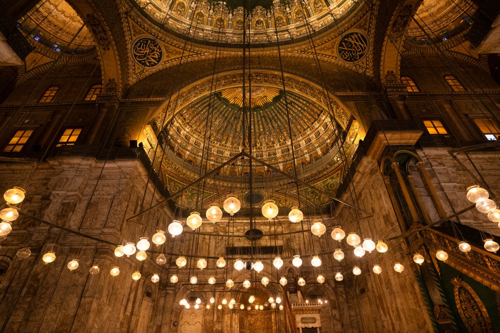 Rows of glowing lamps beneath a richly decorated mosque dome.