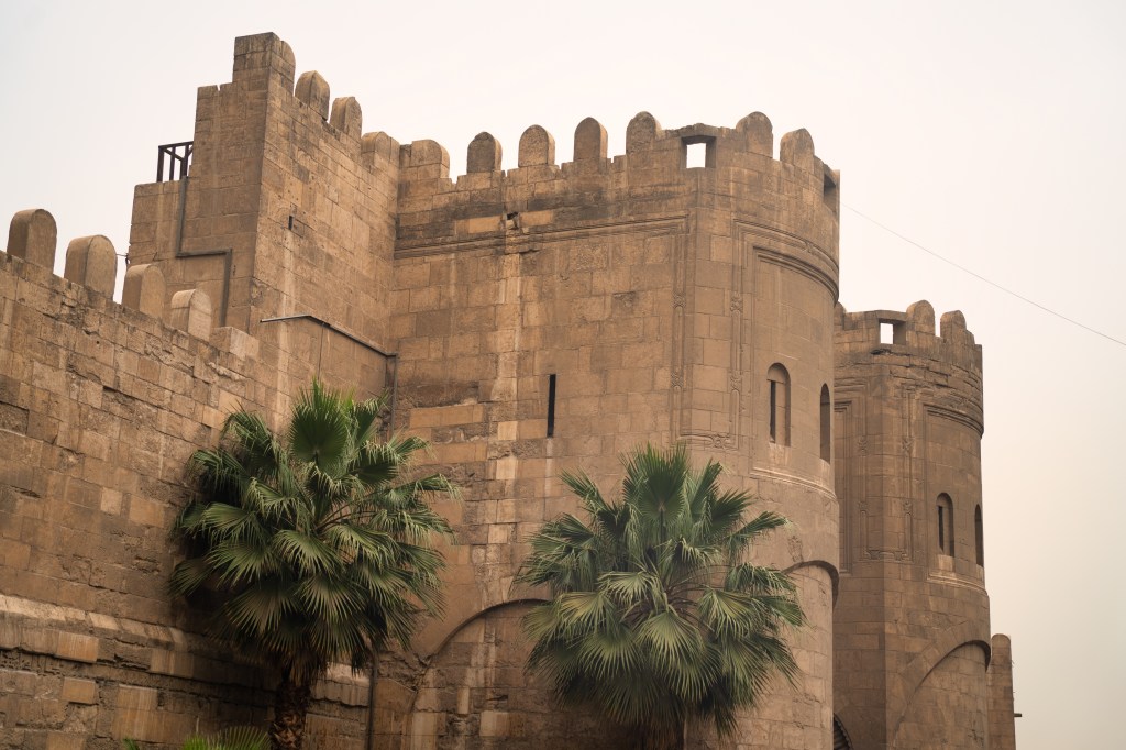 Palm trees beneath a crenellated stone gateway in Cairo.