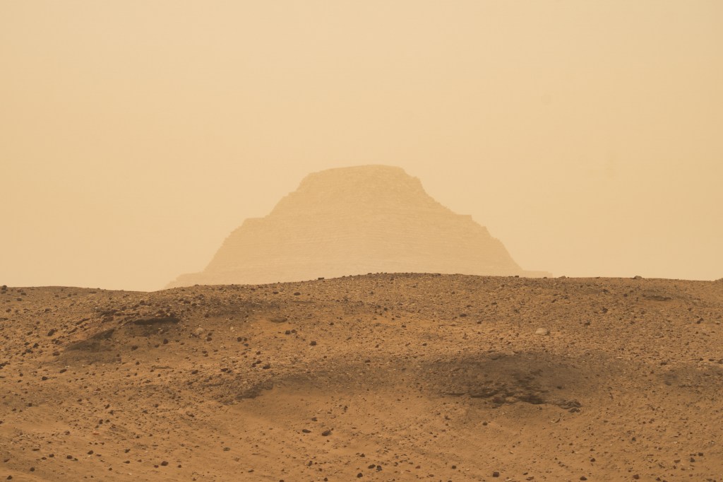 The Step Pyramid appearing faintly through dusty air beyond a low desert ridge.