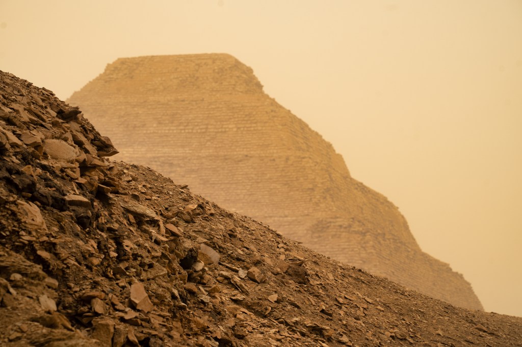 The Step Pyramid rising behind a dark ridge of rough stones.
