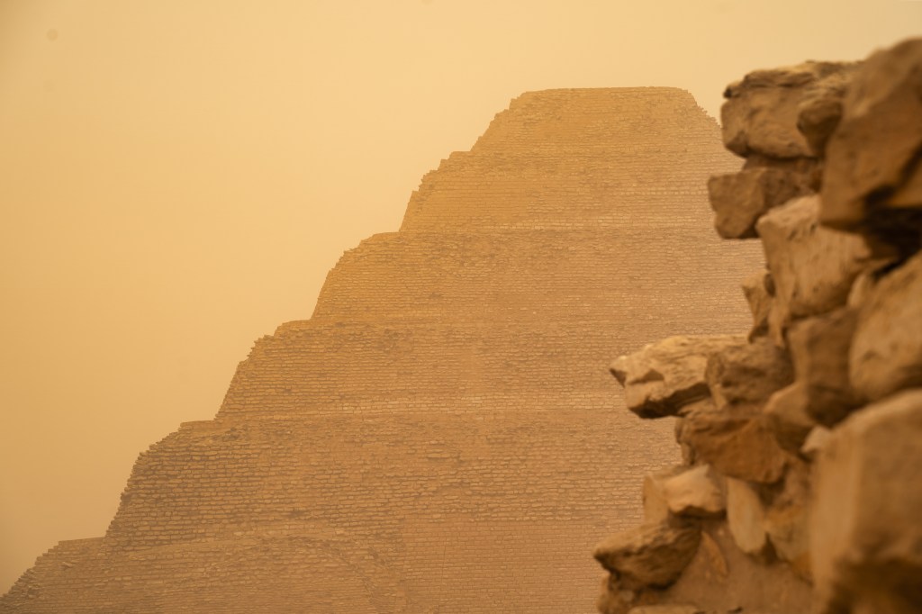 Stepped pyramid partially framed by an old stone wall.