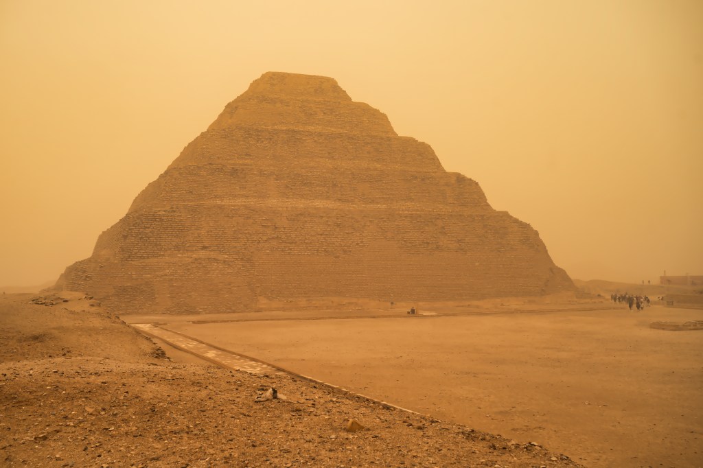 Wide view of the Step Pyramid with a sandy path and tiny visitors nearby.