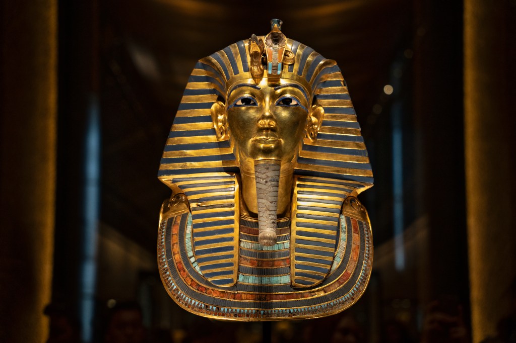 A golden funerary mask with a blue-and-gold striped headdress against a dark background.